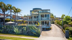 A modern multi-story building with balconies, a mural of tropical plants, and a clear sky. - The Palms Apartments (Merimbula)