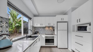 A modern kitchen with white cabinets, a stainless steel oven, and a microwave. - The Palms Apartments (Merimbula)