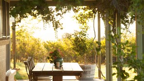 A wooden table with chairs under a pergola, surrounded by greenery and a clear view of a garden. - Rosby Guesthouse (Eurunderee)