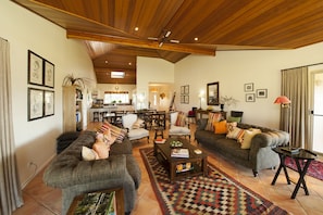 A spacious living room with a high ceiling, wooden beams, and a cozy fireplace. There are multiple seating areas with comfortable sofas and armchairs. - Rosby Guesthouse (Eurunderee)