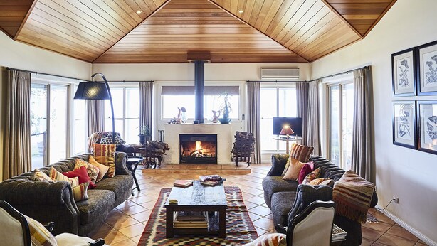 A cozy living room with a fireplace, wooden ceiling, and large windows. - Rosby Guesthouse (Eurunderee)