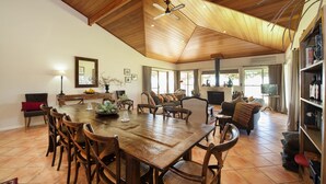 A spacious dining area with a large wooden table and chairs, a ceiling fan, and a view of the outdoors through large windows. - Rosby Guesthouse (Eurunderee)