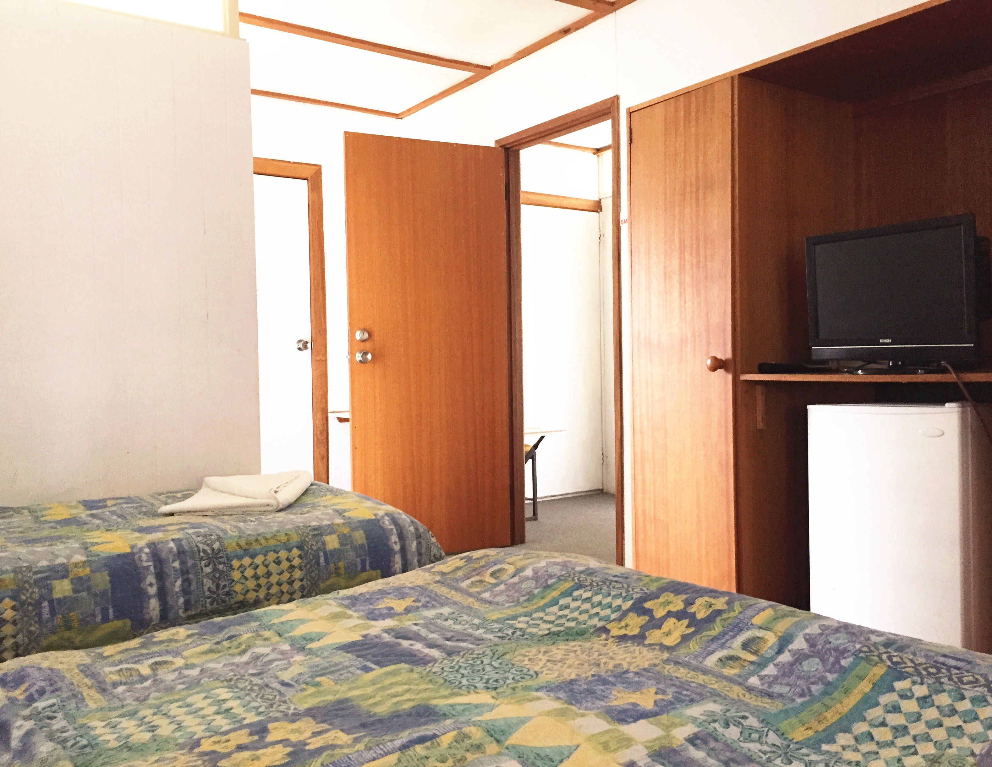 A room with two beds, a television on a shelf, and a refrigerator.