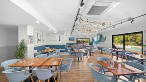 A modern restaurant with wooden tables and light blue chairs, a large mural, and a view of the outdoors.