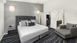 A modern hotel room with a large bed, a gray sofa, a nightstand, and a ceiling fan.