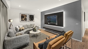 A modern living room with a grey sofa, a tan armchair, a coffee table, and a flat-screen TV mounted on the wall.