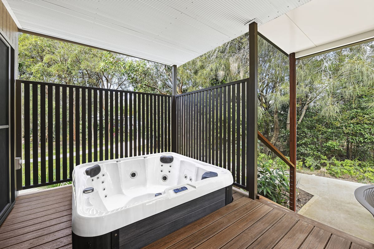 A hot tub on a wooden deck with a view of trees and a fence.