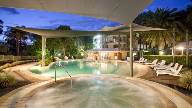 A swimming pool area with lounge chairs and a hot tub, surrounded by a covered patio and palm trees.