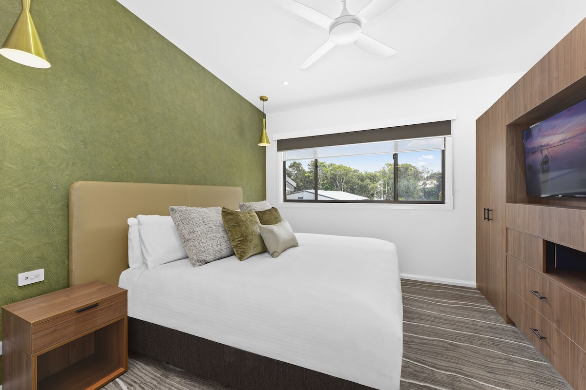 A modern bedroom with a bed, nightstand, and built-in TV cabinet.