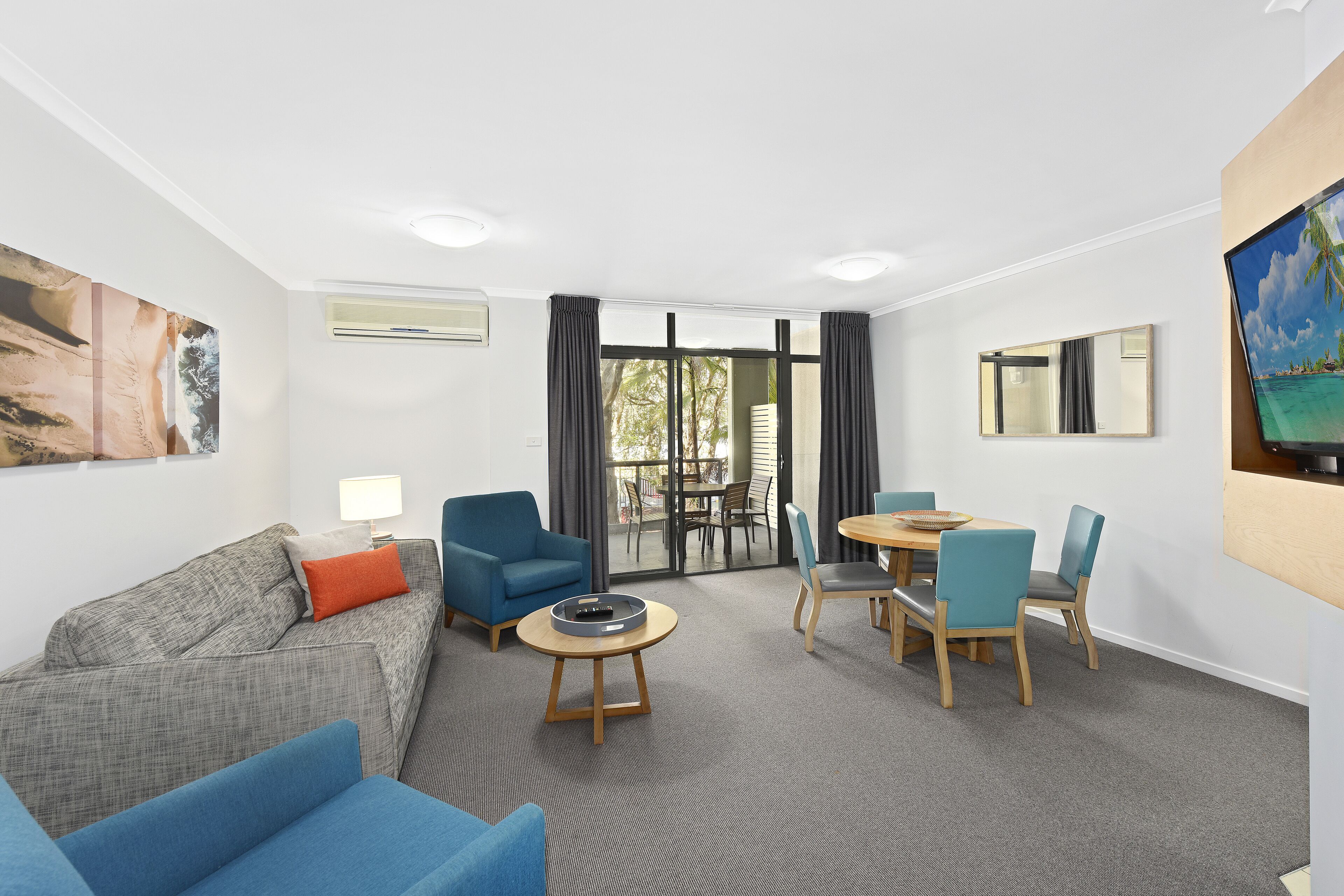 A modern living room with a grey sofa, blue armchairs, a round coffee table, and a dining area with wooden chairs and a table.