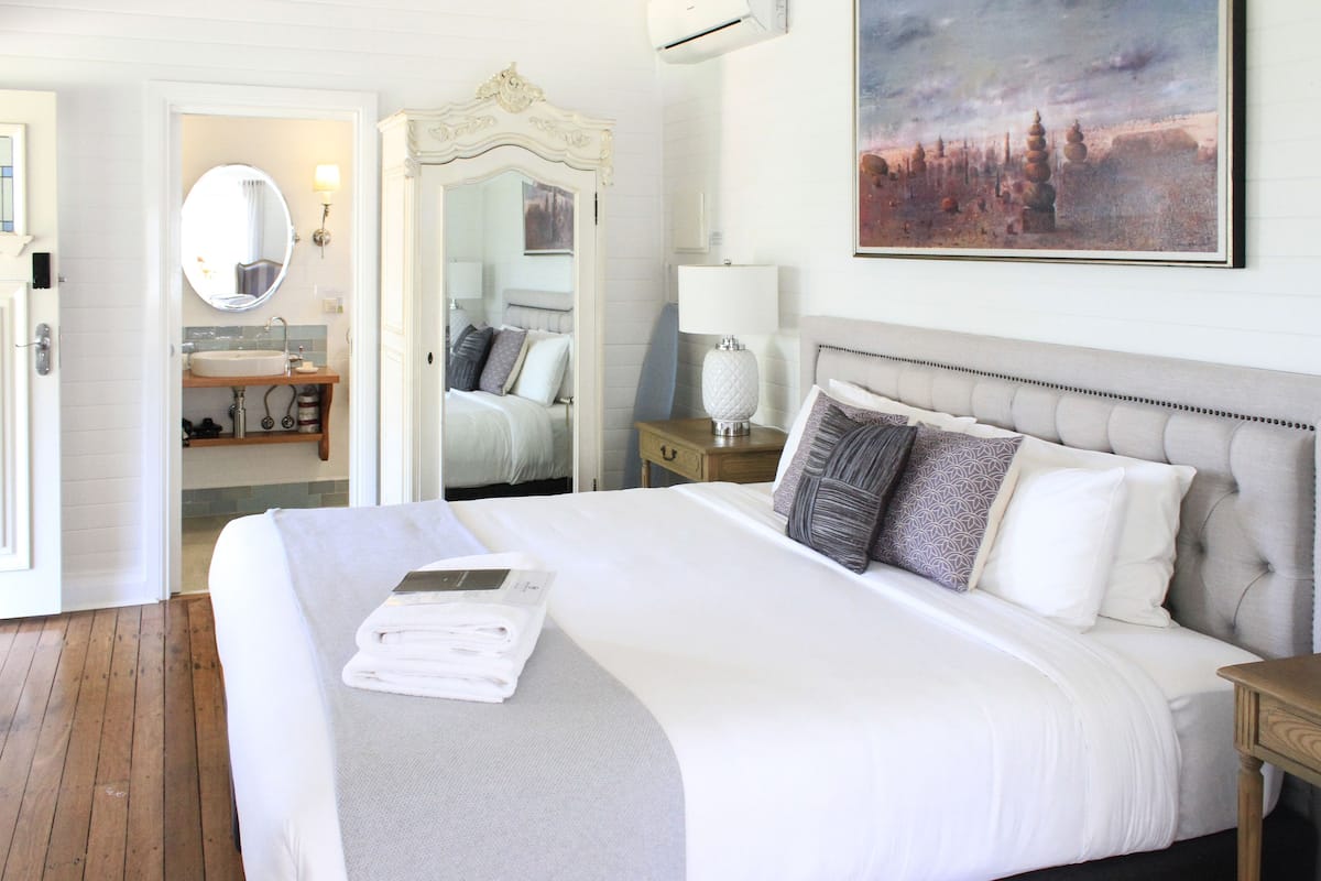 A hotel room with a large bed, a bathroom with a sink, and a painting on the wall.