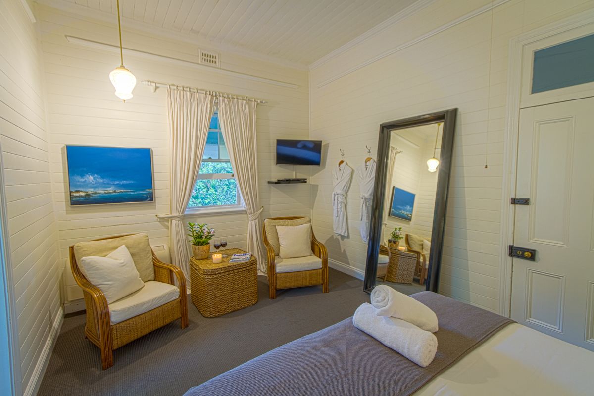 Habitación de hotel con una cama, dos sillones de mimbre, una mesita con una vela, un televisor y una ventana con cortinas.