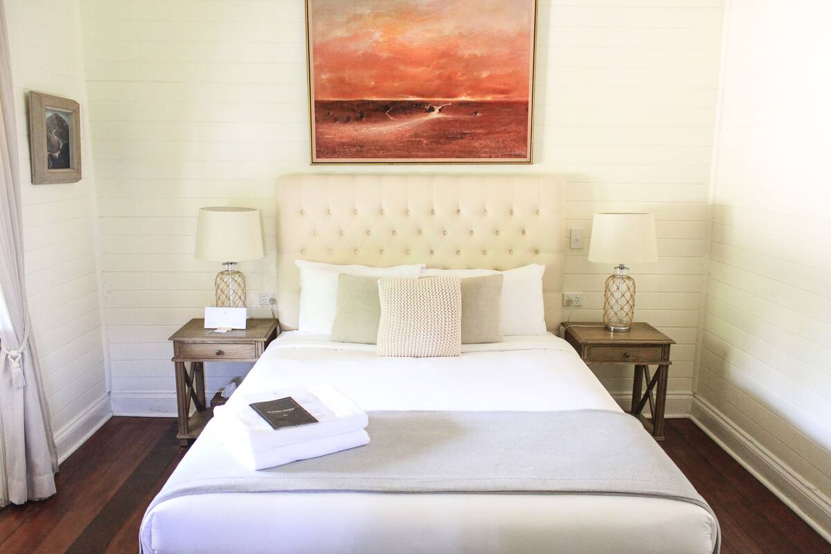 A hotel room with a large bed, two bedside tables with lamps, a painting above the bed, and a small framed picture on the wall.