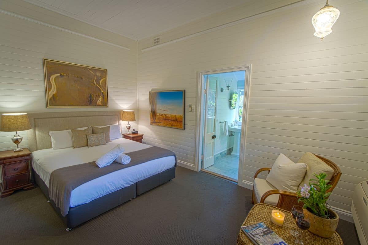 A bedroom with a bed, bedside tables, a lamp, a painting, a chair, a small table with a candle, and a door leading to a bathroom.