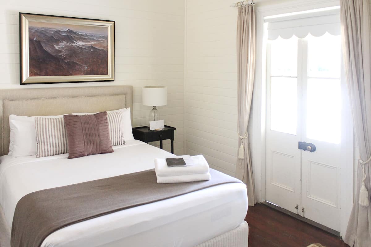 A neatly made bed with a brown headboard, a bedside lamp, and a framed artwork above it.