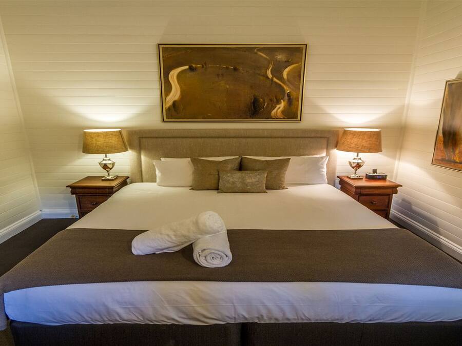 A neatly made bed with a brown headboard, two bedside tables with lamps, and a painting above the bed.