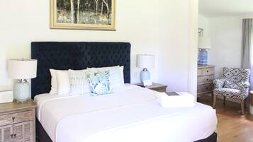 A neatly made bed with a dark headboard, two bedside tables with lamps, a patterned chair, and a framed picture on the wall.