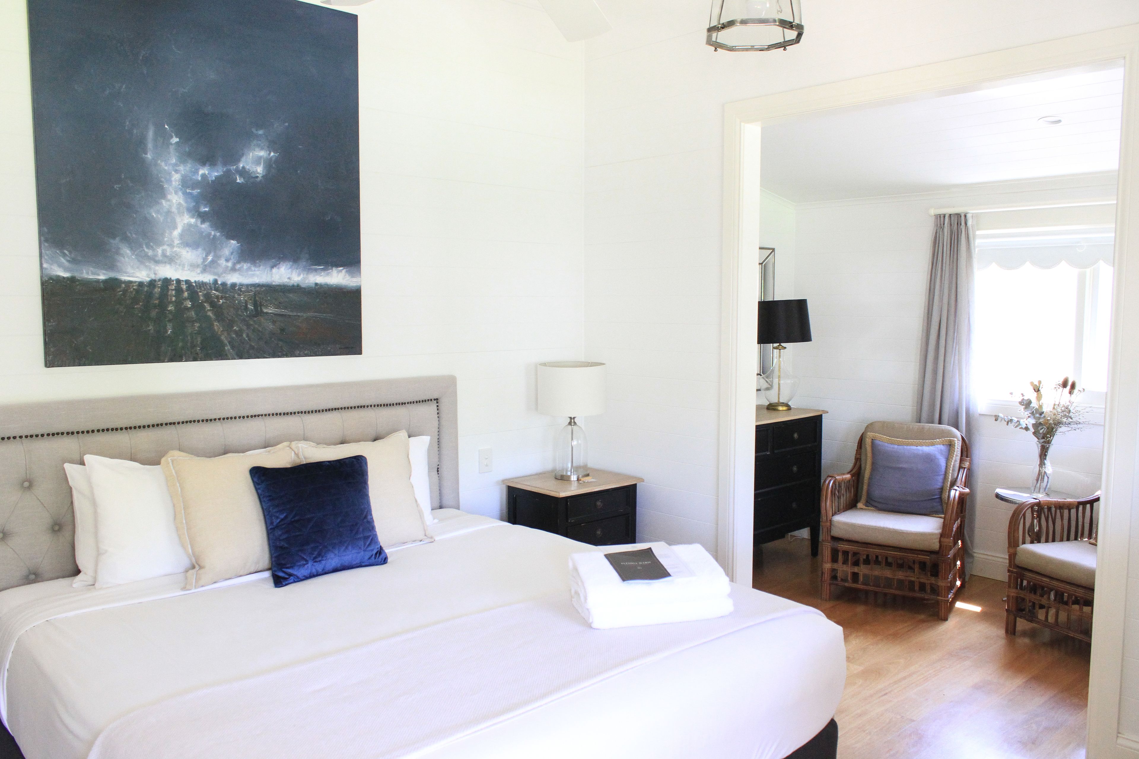 A hotel room with a large bed, a nightstand with a lamp, a chair, and a painting of a stormy sky.