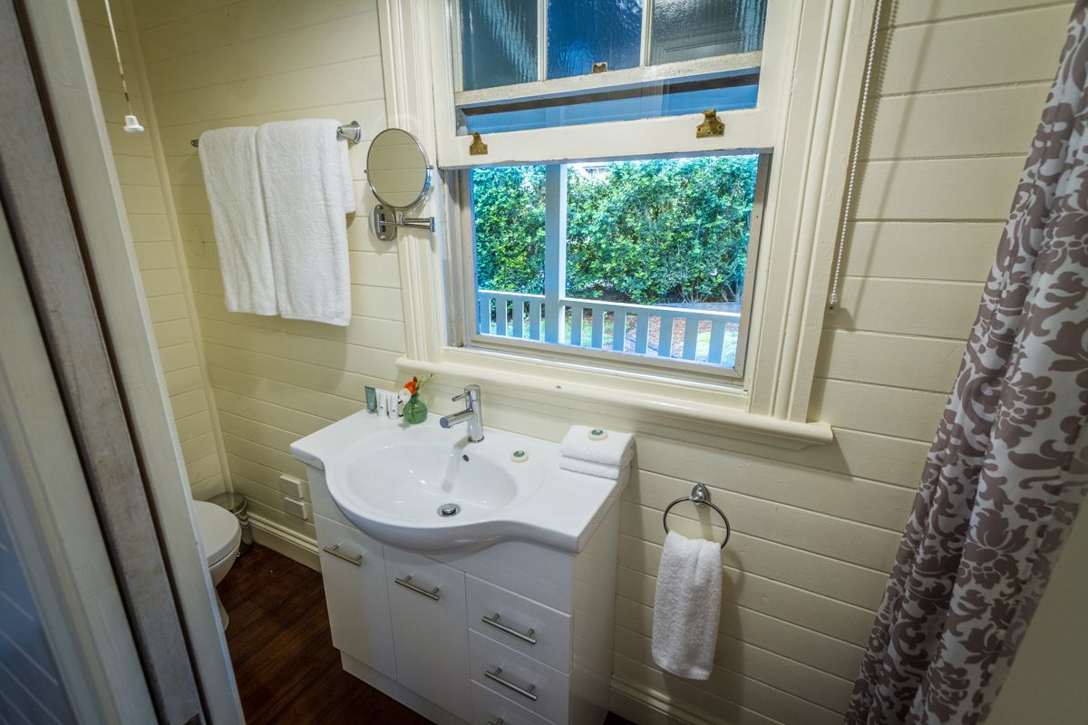 A bathroom with a white sink, a mirror, and a window with a view of greenery.