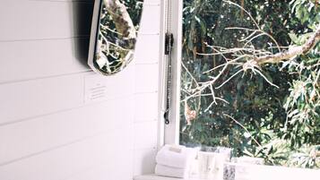 A bathroom with a white sink, a mirror, and a window with a view of trees.