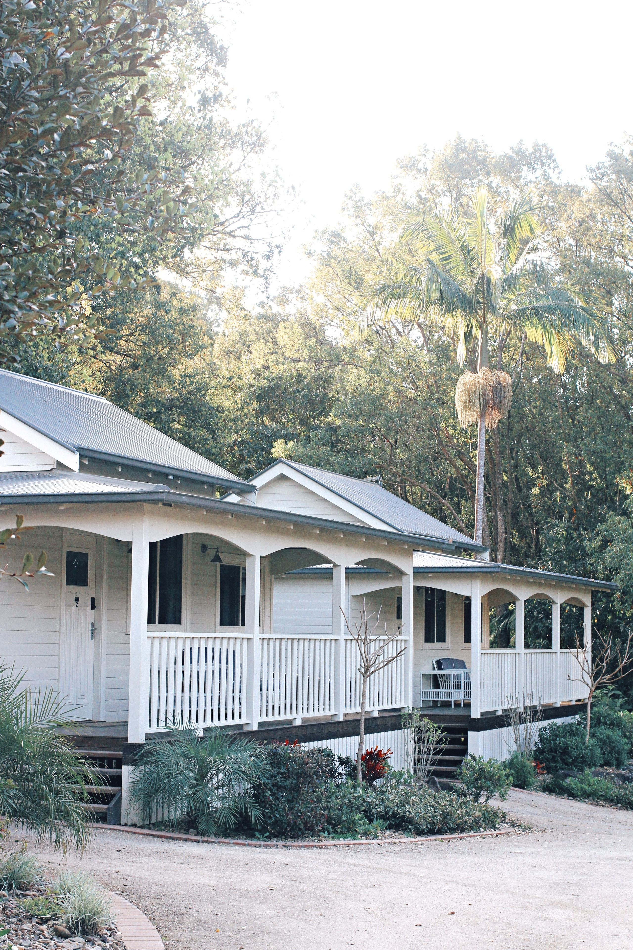 A two-story house with a porch, surrounded by tropical vegetation.