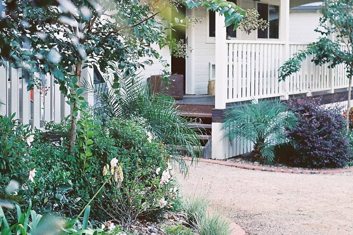 A house with a covered porch, surrounded by various plants and a gravel pathway.