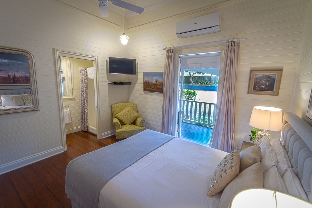 Une chambre à coucher avec un lit, une chaise, une télévision et un balcon avec des rideaux.