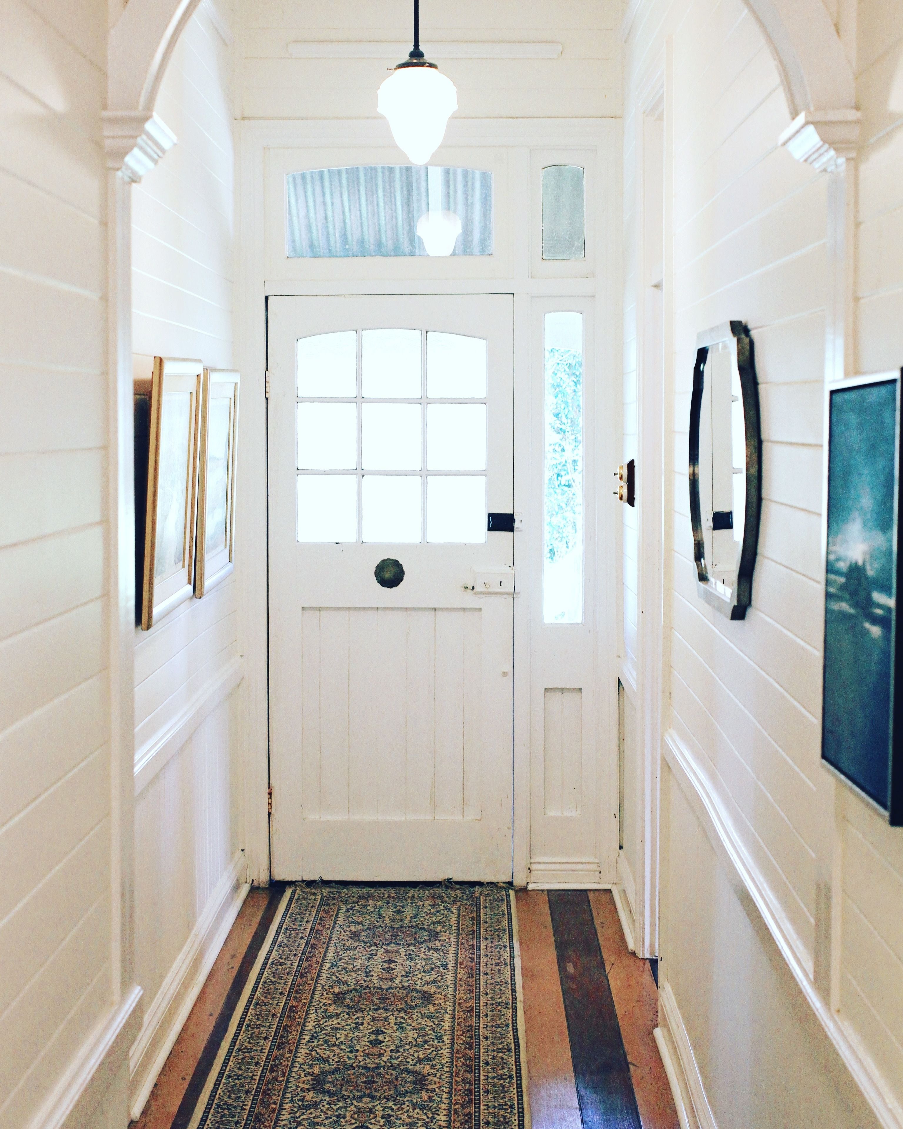 A hallway with a white door, a patterned rug, and framed pictures on the walls.