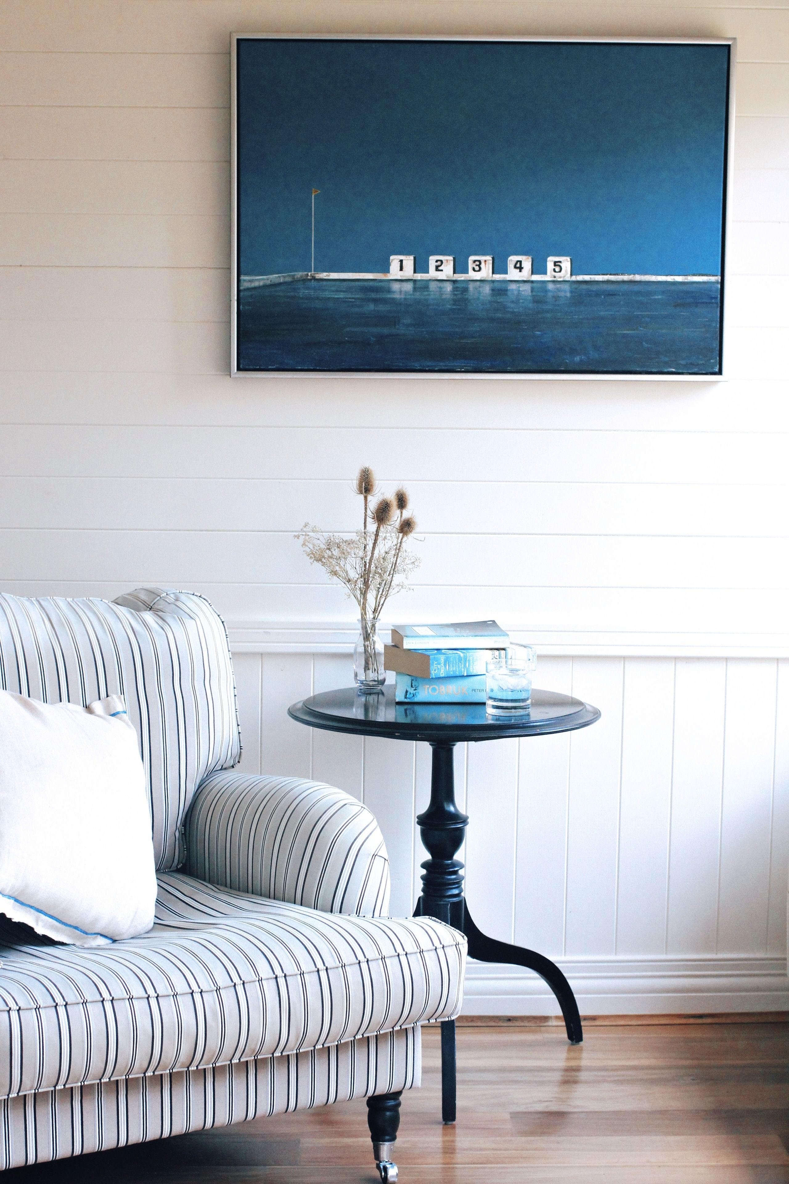 A striped sofa, a small round table with books and a vase, and a framed artwork above.