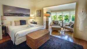 Een slaapkamer met een groot bed, een zithoek met stoelen, uitzicht op groen en een schilderij aan de muur.