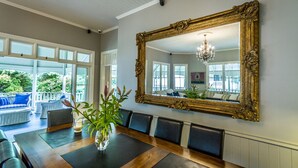 Een eetkamer met een grote, versierde spiegel, een houten eettafel en uitzicht op de omgeving door grote ramen.