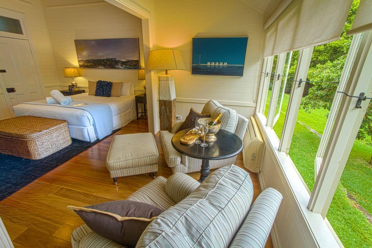 A cozy room with a bed, two sofas, a small table with a lamp, and a view of a green garden.