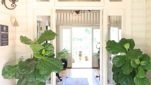 Een hal met een witte deur, twee grote plantenpotten, een vloerkleed en een kroonluchter.
