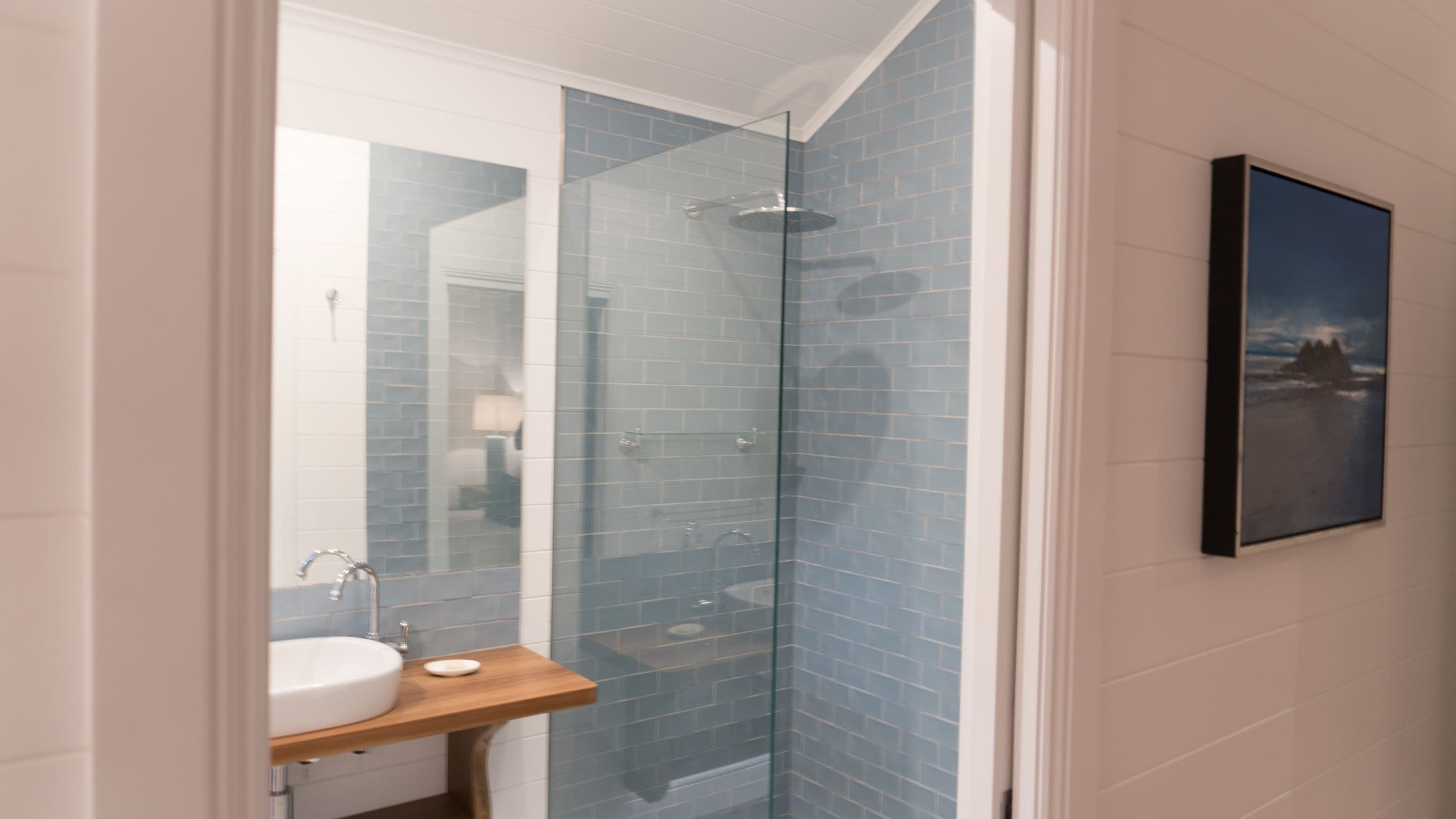A bathroom with a glass shower enclosure, a sink with a wooden countertop, and a framed picture on the wall.