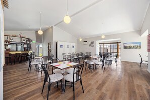 A spacious dining area with multiple tables and chairs, a bar area with shelves of bottles, and large windows providing natural light. - Coal Creek Motel (Korumburra)