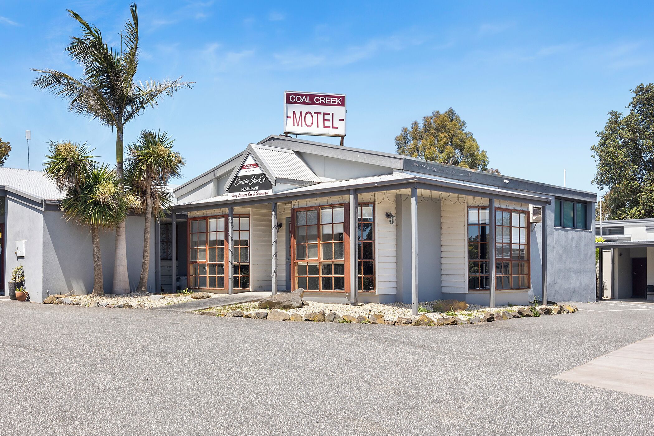 Un motel avec un panneau indicateur, une véranda couverte et un palmier.