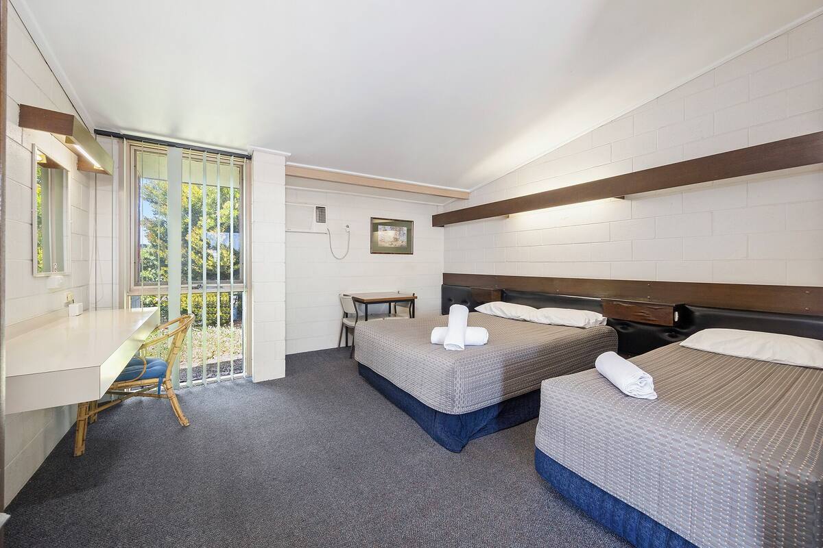 Une chambre d’hôtel avec deux lits, un bureau et un balcon donnant sur un espace verdoyant.