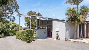 Un espace d’accueil avec un panneau indicateur, un bâtiment moderne et un palmier.