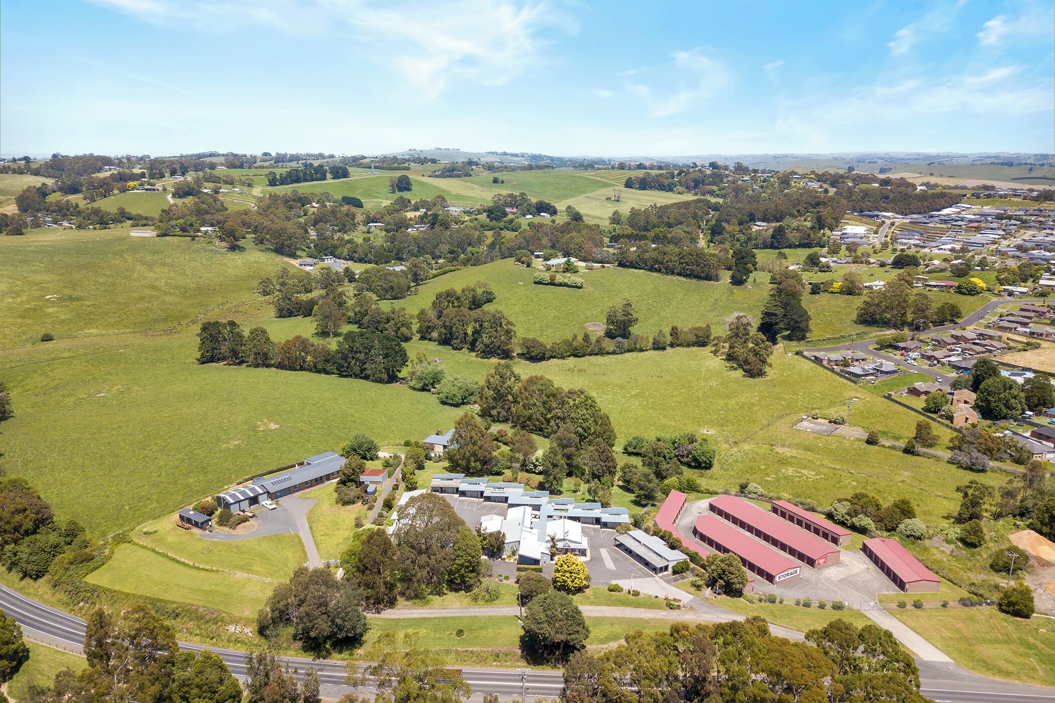 An aerial view of a large industrial complex with multiple buildings, surrounded by green fields and trees.