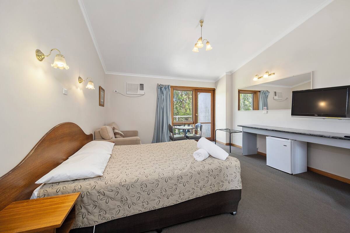 Une chambre d’hôtel avec un lit, un bureau, une télévision et une fenêtre avec des rideaux.