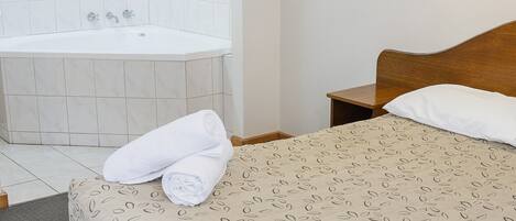 Un dormitorio con techo de madera, una bañera blanca, una cama con colcha estampada, un cuadro enmarcado en la pared y una mesita de noche con lámpara.