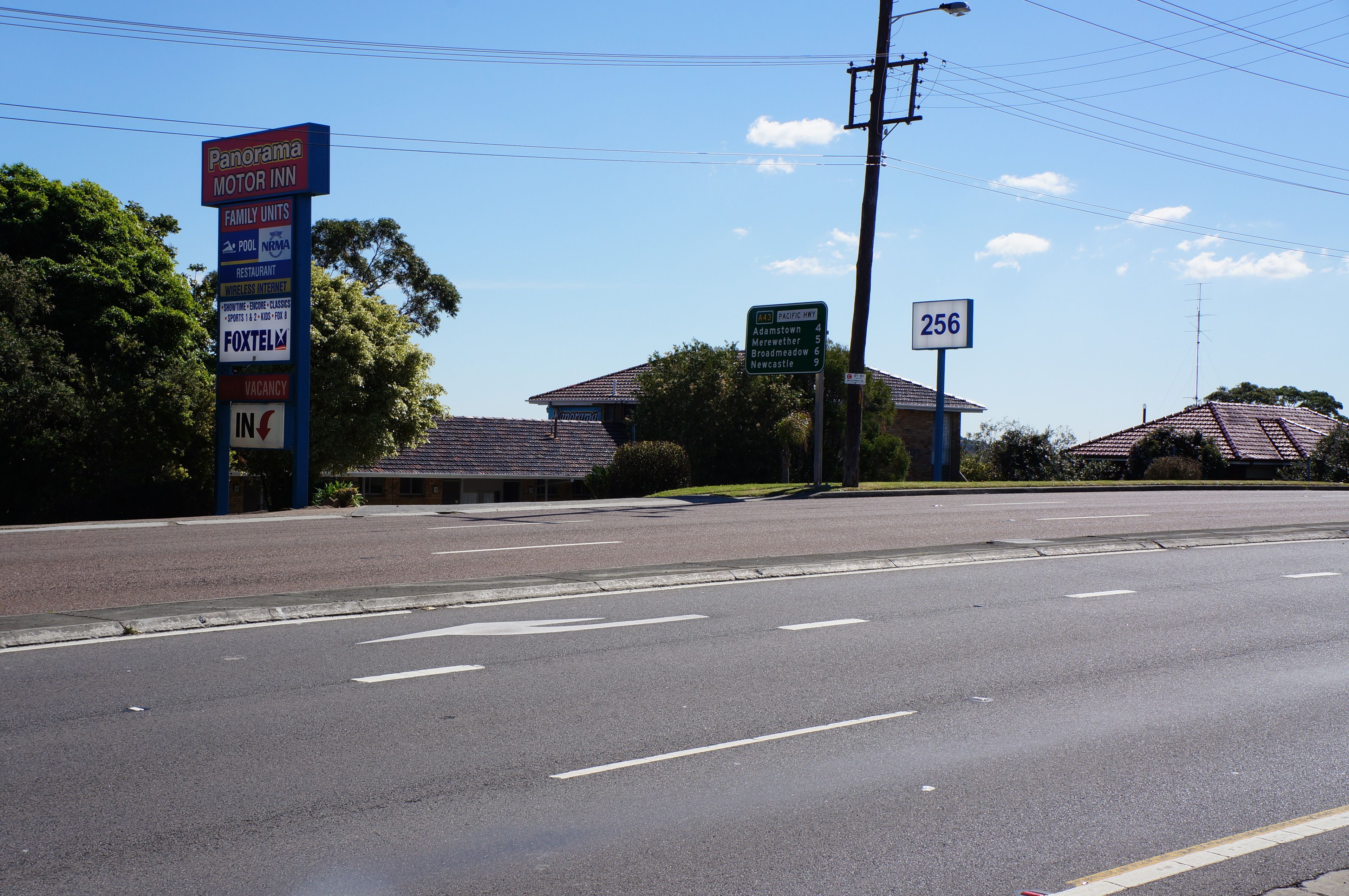 A street view with a motel sign, a road sign, and a building with a tiled roof.