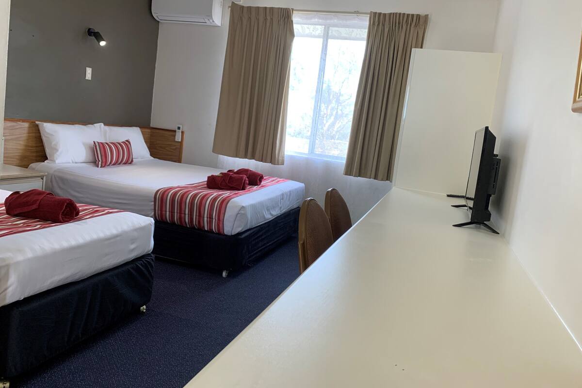 A hotel room with two beds, a desk, a TV, and a window with curtains.