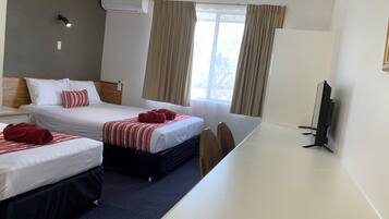 Ein Hotelzimmer mit zwei Betten, einem Schreibtisch, einem Fernseher und einem Fenster mit Vorhängen.