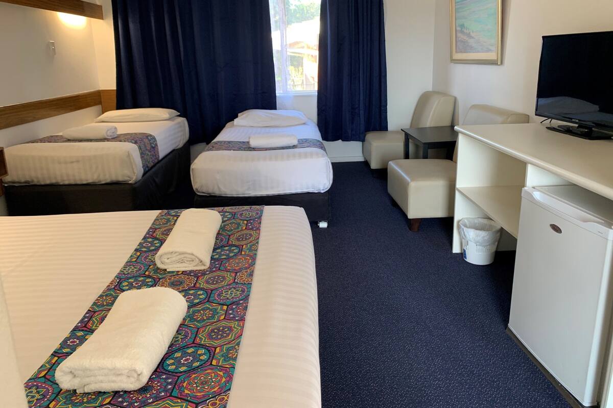 A hotel room with two single beds, a desk with a television, a chair, and a small refrigerator.