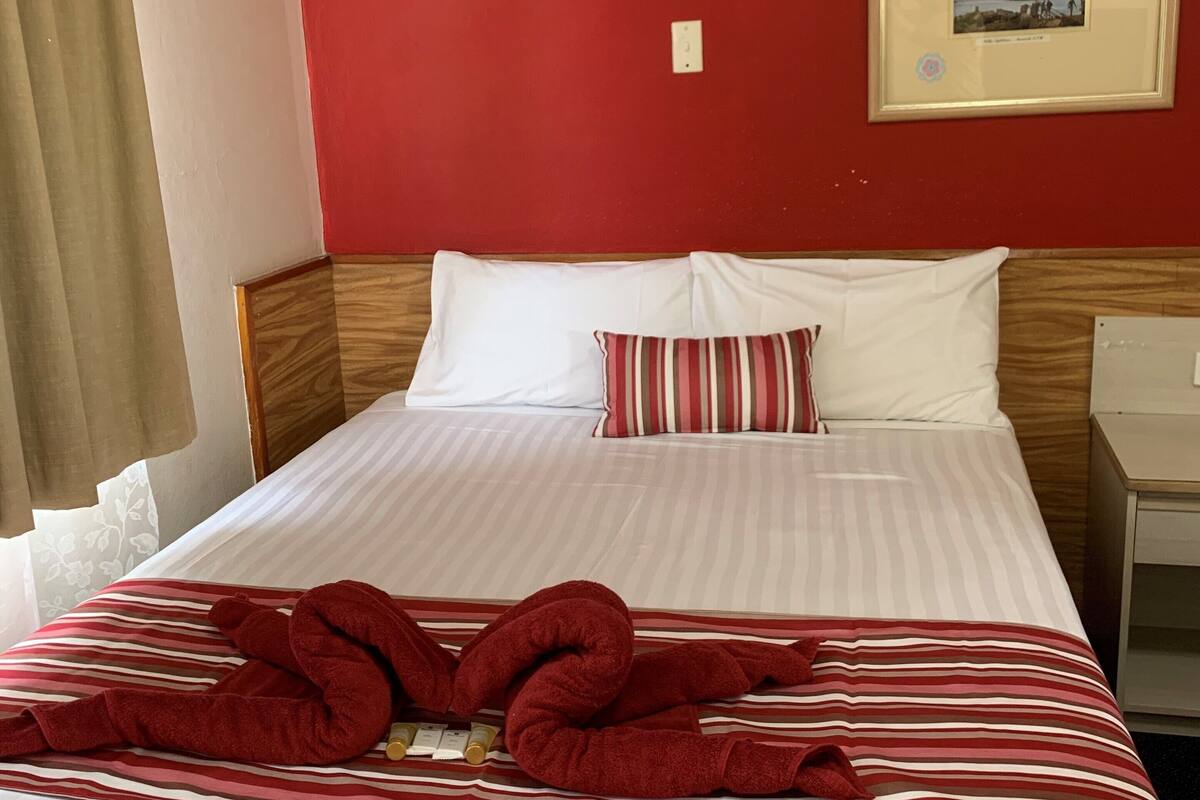 A hotel room with a bed, a framed picture on the wall, and a window with curtains.