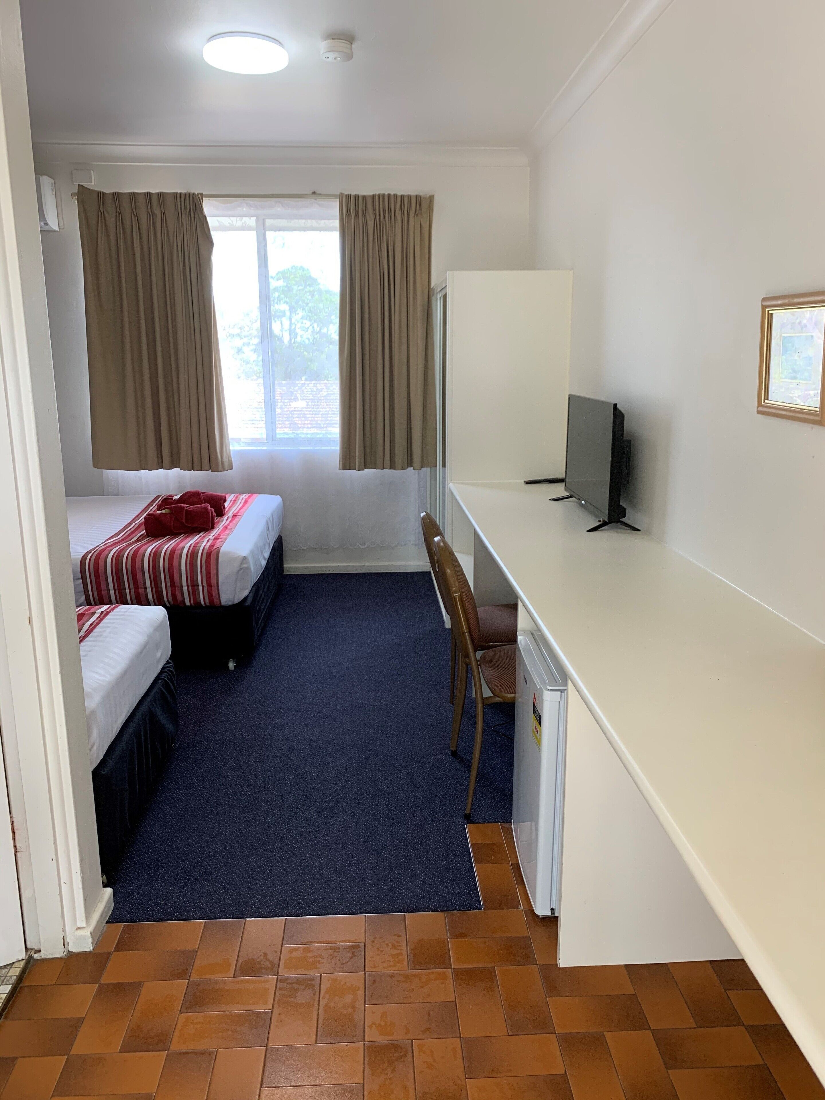 A hotel room with two beds, a desk, a chair, and a television.