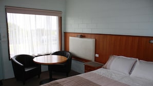 A hotel room with a bed, a round table, two chairs, a wooden headboard, and a window with curtains.