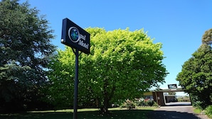 A sign for the Opal Motel with a clear view of the surrounding greenery and a building in the background.