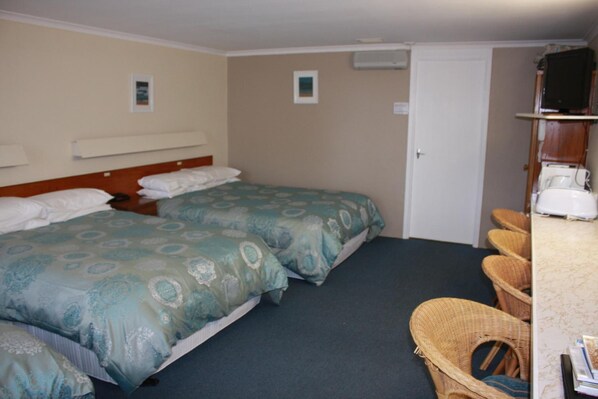 A room with two beds, a small table, wicker chairs, and a television on a stand.